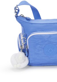 Borsa a tracolla in nylon azzurro chiaro con superficie testurizzata, cerniere bianche, un'etichetta con logo e un portachiavi a forma di scimmia in pelliccia bianca.