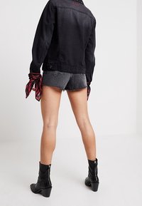 Czarna kurtka dżinsowa, szare poszarpane szorty, czerwona kraciasta chusta związana na nadgarstku, czarne botki na obcasie. Skupienie na casualowym stylu ulicznym i teksturach.