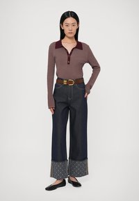 Brun ribbad långärmad topp med vinröd krage och knappar, ihop med mörk denimjeans med vida ben, mönstrade muddar och guldfärgade detaljer.