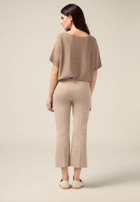Bronzen gebreide top met brede mouwen, gecombineerd met lichtbeige op maat gemaakte broek. Punten flats met een crèmekleurige afwerking maken de look compleet.
