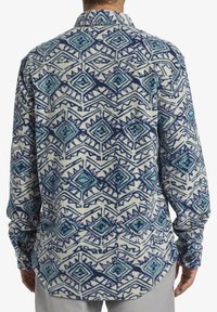Fleece skjorte i et geometrisk mønster med blå, teal og lilla nuancer på en cremefarvet baggrund; har en klassisk krave og lange ærmer.