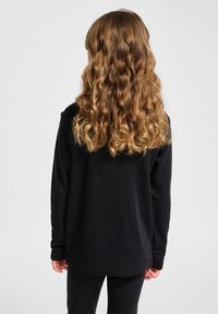 Schwarzes Langarmshirt mit lockerem Schnitt, aus weichem Stoff. Mit gerippten Bündchen und abgerundetem Saum, kombiniert mit passenden schwarzen Hosen.