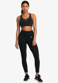 Musta urheiluliivi logolla ja korkeavyötäröiset mustat legginsit, molemmat joustavasta kankaasta, tiiviisti istuvia ja minimalistisella suunnittelulla.