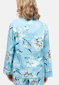 Conjunto de pijama azul con flores grandes de color blanco y centros amarillos. Tejido suave, mangas largas y ajuste relajado con un diseño floral detallado.