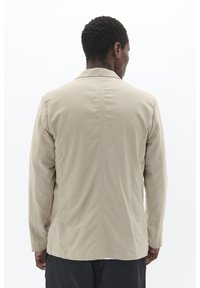 Beige, long-sleeved jacket with a straight silhouette, featuring a classic collar, subtle texture, and minimal stitching details on the back.