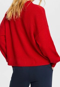 Roter übergroßer Strickpullover mit strukturierter Oberfläche, runder Halslinie und überschnittenen Schultern. Der Saum ist gerippt und endet auf Taille.