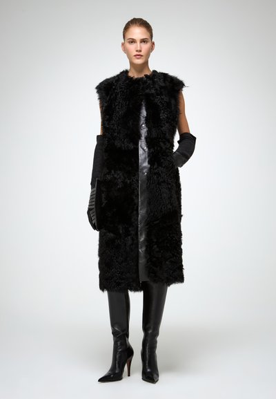 Gilet in pelliccia nera con pannelli in pelle, design senza maniche e colletto alto. Il modello indossa guanti lunghi neri e stivali con tacco a spillo alti fino al ginocchio.