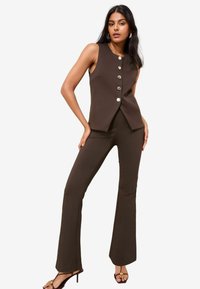 Brauner ärmelloser Top mit silbernen Knöpfen, kombiniert mit einer schmal geschnittenen braunen Schlaghose. Glatte Struktur und maßgeschneiderter Schnitt für einen harmonischen Look.