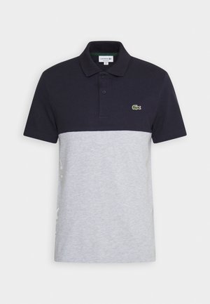 Kortærmet polo med sort øverste halvdel, lysegrå nederste halvdel, to knapper, krave og lille grønt krokodillelogo på brystet.