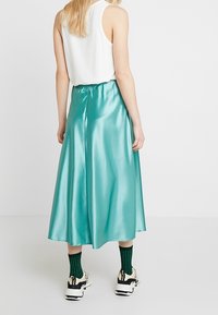 Středometrická sukýnka z lesklého tyrkysového saténu s elastickým pasem, doplněná o bílé tenisky a zelené pruhované ponožky.