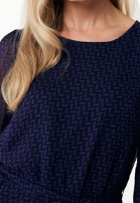 Vestido navy con un patrón geométrico texturizado en púrpura oscuro. Mangas largas, escote redondo y una cintura ceñida para una silueta ajustada.