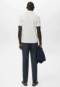 Bijela kratka polo majica, slim fit, u kombinaciji s tamnoplavim elegantnim hlačama. Nosite s sandalama, držeći tamnoplavi sako.