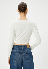 Witte geribbelde lange mouw top met een cropped ontwerp, gecombineerd met loszittende donkere denim jeans met achterzakken en een leren patch.