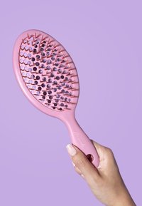 Brosse à cheveux rose avec une poignée texturée, une tête ovale et des trous ouverts entre les poils pour réduire les accrochages. Finition lisse et design léger.