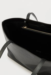 Černá kožená taška přes rameno s dvěma uchy. Vnitřek obsahuje přihrádku na zip a hladkou texturu. Minimalistický design s čistým tvarem.