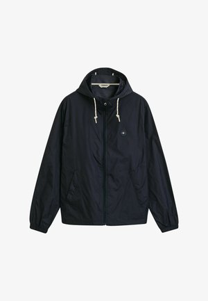 Chaqueta ligera azul marino con capucha, cordones, cremallera frontal, puños elásticos y dos bolsillos laterales. Presenta un logotipo circular en el pecho.