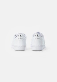 White sneakers made of smooth leather with a low-top silhouette, featuring a textured side panel and a metallic logo on the heel.