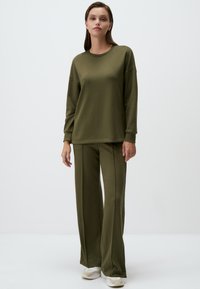 Olijf groene loungewear set met een relaxte lange mouw top en wijde broek, gemaakt van zachte stof met een gladde textuur.