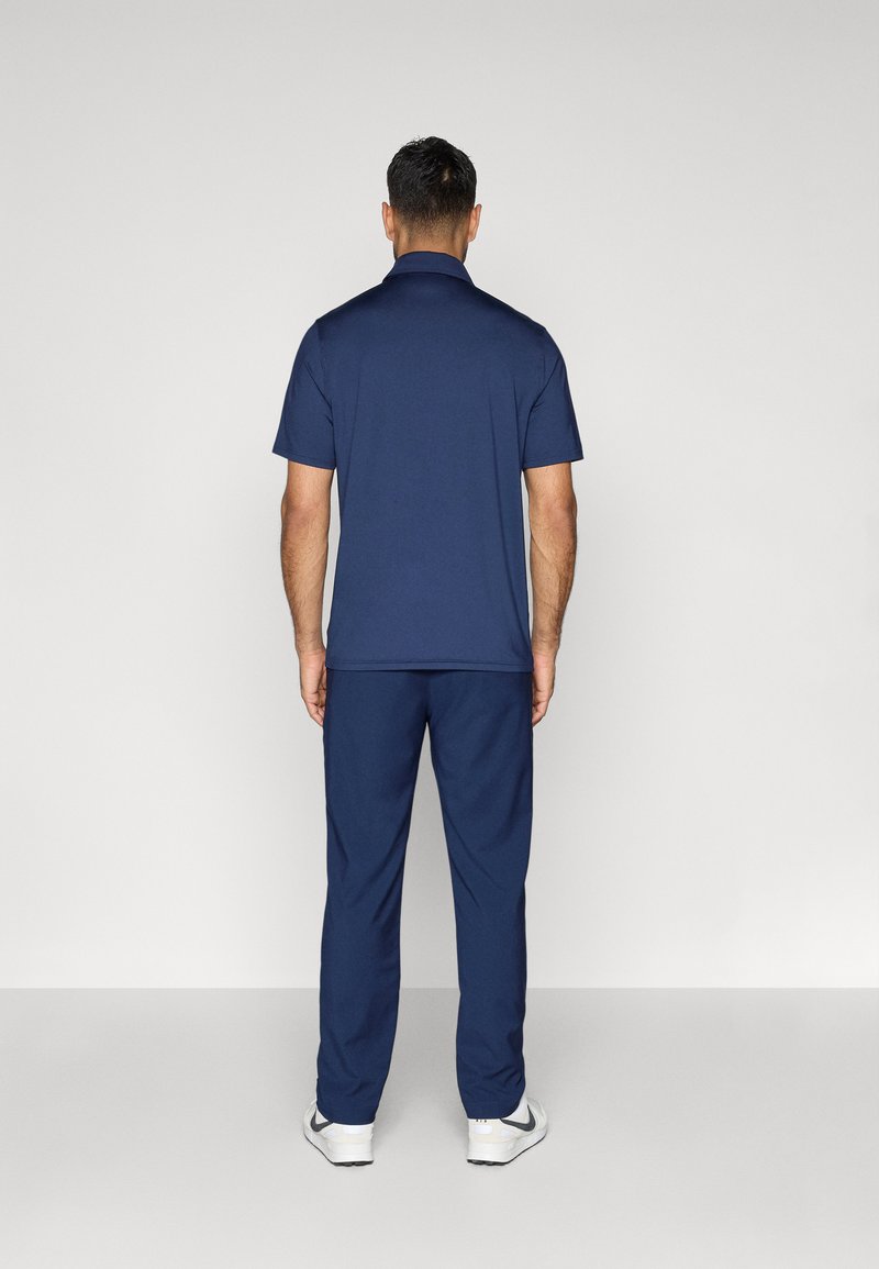 Blaue Polo- und Hosenkombination aus weichem Stoff. Das kurzärmelige Polo hat einen Kragen; die Hose ist gerade geschnitten. Sneakers runden das Outfit ab.