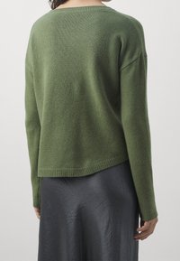 Maglione a maniche lunghe in verde oliva, formaggio morbido, con scollo rotondo e orlo a costine. Abbinato a una gonna lucida grigio antracite.