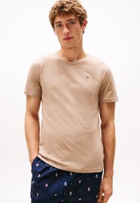 T-shirt in cotone beige con maniche corte, scollatura rotonda e un piccolo logo. Indossato con pantaloni corti blu navy con motivi colorati.