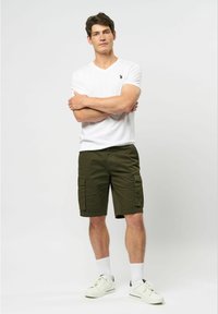 Tricou alb cu guler în V, asortat cu pantaloni scurți cargo de culoare verde măsliniu, care au buzunare laterale. Modelul poartă adidași albi și șosete albe până la glezne.