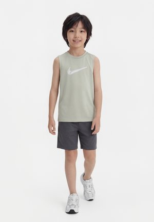 Niño caminando hacia adelante con una camiseta sin mangas verde menta de Nike, pantalones cortos gris oscuro y zapatillas blancas sobre un fondo blanco liso.