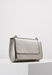 Metaliczna srebrna torebka o teksturowanej powierzchni, prostokątnym kształcie, z podwójnym łańcuszkiem jako paskiem i klapką z przodu do zamknięcia.