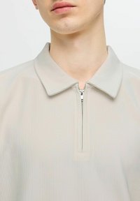 Světle šedá zipová košile s límečkem, ribbed texturou a krátkým zipem vpředu, navržená pro přiléhavý vzhled.