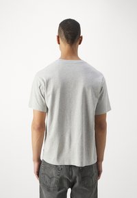 Grå bomuld t-shirt med korte ærmer, rund hals og lige kant, parret med mørk grå jeans. Ingen synlig branding eller mønstre.