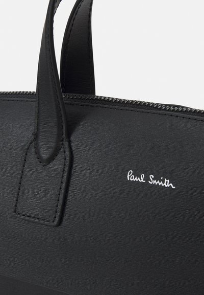 Sort læderhåndtaske med struktureret overflade, der har to håndtag og et sølvfarvet "Paul Smith" logo. Detaljer med lynlåslukning synlige.