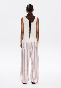 Haut sans manches blanc, écharpe en tricot marron, et pantalon ample rayé avec poches. Le tissu a une texture légère, avec des rayures verticales rouges et bleues.