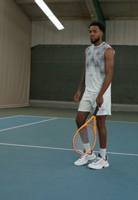 Camisola técnica branca com um padrão texturizado, calções combinando e uma raquete de ténis laranja. Os sapatos são brancos com detalhes em preto e cinza.