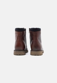 Hnědé kožené kotníkové boty s texturovaným povrchem, černým elastickým límcem, bočním zipem a robustní hnědou podrážkou.