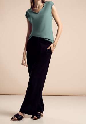 Sininen V-kaula-aukollinen toppi, rento istuvuus; mustat leveälahkeiset housut taskuilla; mustat liukusandaalit. Sileä pinta, moderni muotoilu. Minimalistinen tyyli.