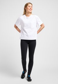 T-shirt blanche en coton avec une poche poitrine, des manches courtes et une coupe décontractée, associée à un jean skinny noir et des baskets noires avec des accents bleus.