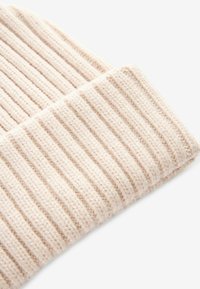 Strickmütze in Creme mit gerippter Textur, umgeschlagenem Rand und weichem Material. Kompakte Form mit gleichmäßigen Nähten und ohne Verzierungen.