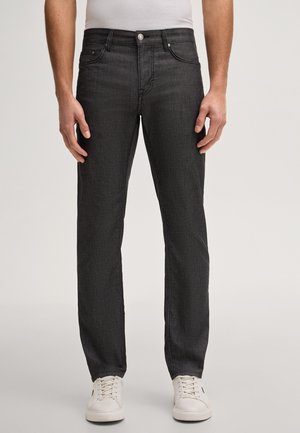 Uomo che indossa jeans neri slim fit con tasche frontali e sneakers bianche su sfondo chiaro.