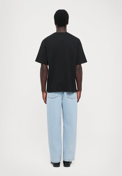 T-shirt en coton noir avec une coupe décontractée, des manches courtes et un col rond, associé à un jean droit bleu clair et des chaussures noires.