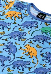 Vaaleansininen luomupuuvillapaita, jossa on leikkisä kuvio apinoista sinisessä, oranssissa ja vihreässä, jotka vuorovaikuttavat banaanimotiivien kanssa.