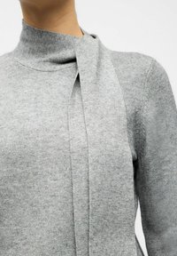 Grauer Pullover mit einem hohen Kragen und einem fließenden, gewickelten Bindeband am Kragen. Weiche Textur und gestrickter Stoff.