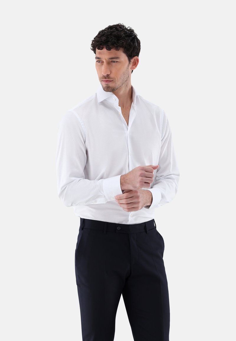 Camicia bianca con una delicata fantasia a quadri, maniche lunghe e colletto a bottoni, abbinata a pantaloni scuri. Vestibilità pulita e sartoriale.