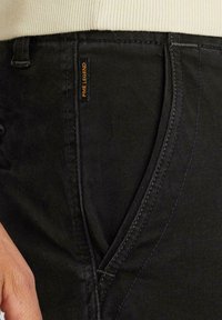 Schwarze Denim-Hosen mit Reißverschluss, orangefarbenem " PME Legend"-Label und sichtbaren Nähdetails. Strukturiertes Material mit schmalem Schnitt.
