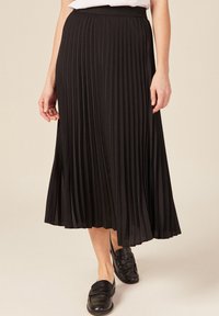 Gonna midi plissettata nera con vita elastica, caratterizzata da profondi pieghe verticali e una texture liscia, abbinata a mocassini neri.