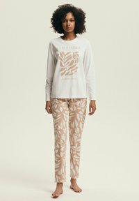 Biała bluzka z długim rękawem z roślinnym nadrukiem w kolorze brzoskwini, zestawiona z beżowymi spodniami z białymi wzorami liści. Miękka, lekka bawełniana tkanina.