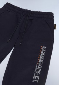 Mørkeblå sweatpants med elastisk talje, snorpå træk, sidelommer og trykte logoer i hvid og orange på venstre ben.