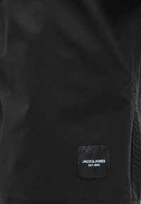 Bermude negre dintr-un material neted, având un eticheta cusută cu "JACK & JONES EST. 1990" în alb, situată în partea stângă jos.