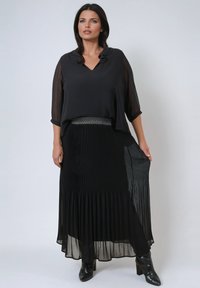 Zwarte blouse met een gerimpelde halslijn, doorzichtige driekwartmouwen. Plissé zwarte maxi rok met een textuur tailleband. Zwarte hakkenlaarzen.