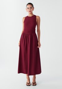 Burgundia värvi varrukateta kleit, millel on lõhikuga korsett ja kogutud seelik, valmistatud siledast kangast, millel on tekstuuriga vöökohal detail ja õrn voog.