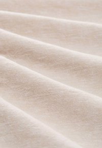 Tela de lino beige claro con una superficie texturada, mostrando suaves pliegues y sutiles variaciones en el color, enfatizando las fibras naturales.